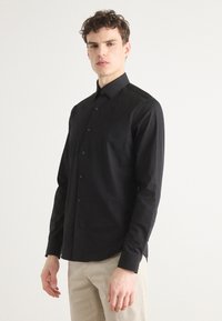 Black button-up shirt with a structured collar and long sleeves. Made from smooth fabric featuring subtle texture. Tailored fit with buttons visible.