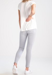 Jeans ajustados de color gris claro con un corte de tiro medio, hechos de denim, combinados con una blusa blanca de manga corta y zapatillas blancas.