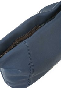 Bolso de tela texturizada azul marino con cierre de cremallera, que cuenta con un interior de cuero marrón y un detalle trenzado en la tirador de la cremallera.