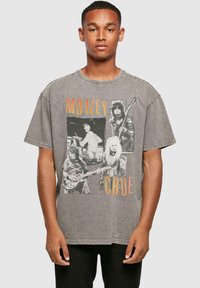 Grå oversized t-shirt med et vintage sort-hvidt grafisk motiv af rockbandmedlemmer, med orange "MÖTLEY CRÜE" tekst på forsiden.