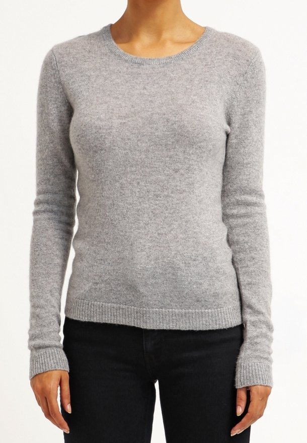 Femme portant un pull ajusté en maille gris clair à manches longues avec des poignets et un ourlet côtelés, associé à un pantalon noir.