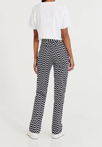 Camiseta blanca recortada de mangas cortas, combinada con pantalones de patrón ondulado en blanco y negro, con una cintura ajustada y piernas acampanadas.