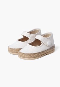White canvas shoes with a round toe, elastic strap, and woven jute-like sole. Features a smooth texture and breathable design.