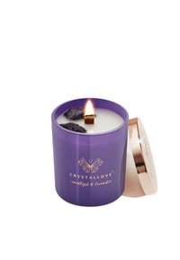 Fioletowa świeca z złotym logo, ozdobiona kryształami ametystu i lawendą, z zapaloną knotem. Okrągły szklany pojemnik, z wyjmowaną złotą pokrywką.