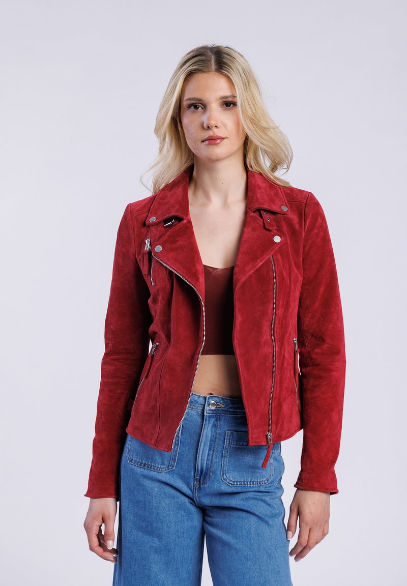 Chaqueta de motorista de ante rojo con bolsillos con cremallera, cuello de presión y diseño ajustado. Combinada con pantalones de mezclilla de cintura alta.