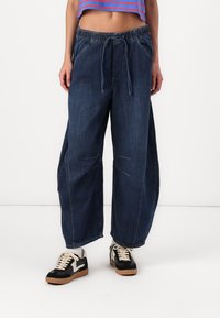 Wide-leg dark denim pants with an elastic waistband, external drawstring, and front pockets. Smooth texture with minimal decorative stitching.