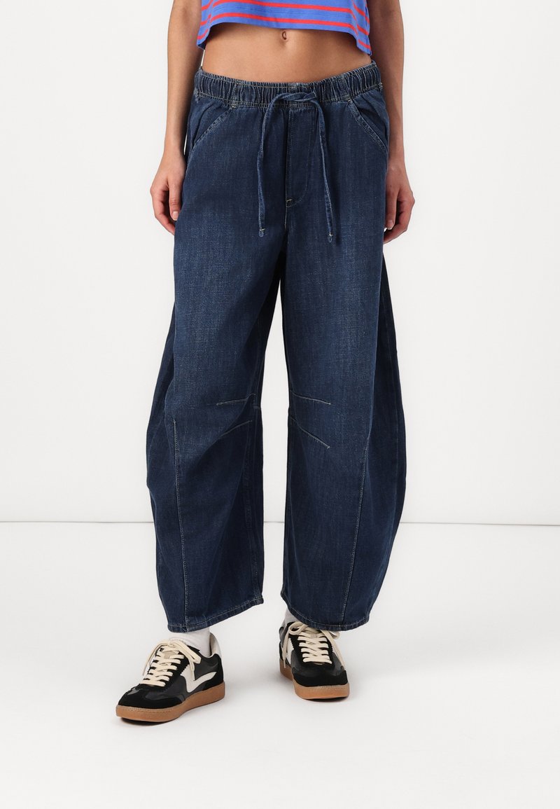Weite Jeans mit elastischem Bund, externem Kordelzug und seitlichen Taschen. Glatte Textur mit minimaler dekorativer Naht.