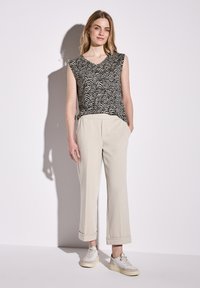 Top senza maniche a righe in bianco e nero abbinato a pantaloni beige a sigaretta, dotati di tasche laterali e risvolti. Sneakers bianche completano l'outfit.