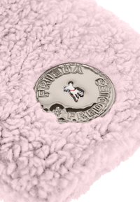 Roze harige stof met een cirkelvormig metallic logo waarop de tekst "FRIEDA" staat en een zilveren hondenfiguur in het midden. Zachte, gestructureerde oppervlakte.