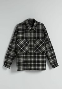 En svart- och vitrutig skjortjacka i flanellmaterial som har två bröstfickor och en knapplist med klassisk krage.