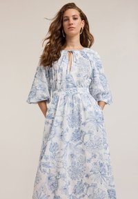 Floral dress in white fabric with blue line drawings. Features a keyhole neckline, gathered waist, and bell sleeves. Pockets included.