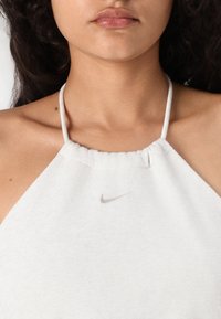 Bijela halter majica izrađena od mekog materijala, s nabranim izrezom i malim srebrnim Nike logotipom na grudima.