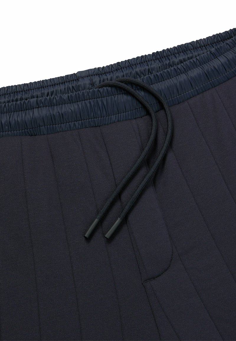 Jogging en bleu marine, plissés, avec une taille élastique et un cordon de serrage. Comprend des poches latérales et une texture lisse.