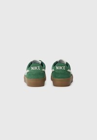 Baskets en suede vert avec une semelle en caoutchouc brun texturé, ornées d'accents de logo blancs à l'arrière et sur le côté.