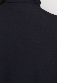 Granatowa teksturowana tkanina z wysokim kołnierzem i subtelnymi detalami przeszyć, prezentująca gładki i lekko usztywniony wygląd.