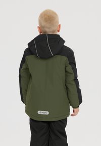 Grön och svart vinterjacka med huva. Tillverkad av slät textil, har reflexdetaljer och en logotypimpregnering vid fållen.