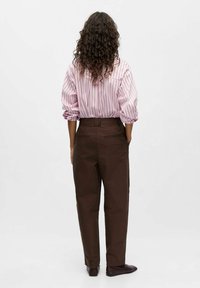 Camicia a strisce rosa chiaro con maniche a sbuffo abbinata a pantaloni marroni. I pantaloni presentano tasche e una vita alta, sottolineando una vestibilità comoda.