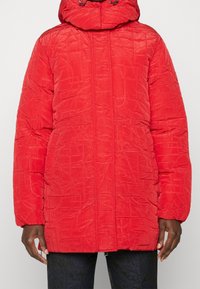 Rode gewatteerde jas met hoge kraag en trekkoordcapuchon. Gestructureerd oppervlak met stikpatronen. Voorzien van een voorrits en zijzakken.