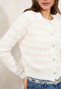 White cardigan with textured knit, featuring pastel horizontal stripes and decorative gem buttons. Ribbed cuffs and waistband, soft material.