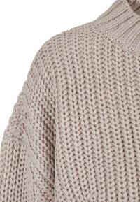 Ljust beige stickad tröja med ribbat krage, med en chunky textur och en lös passform. Delvis visad med en diaganl sömdetalj.