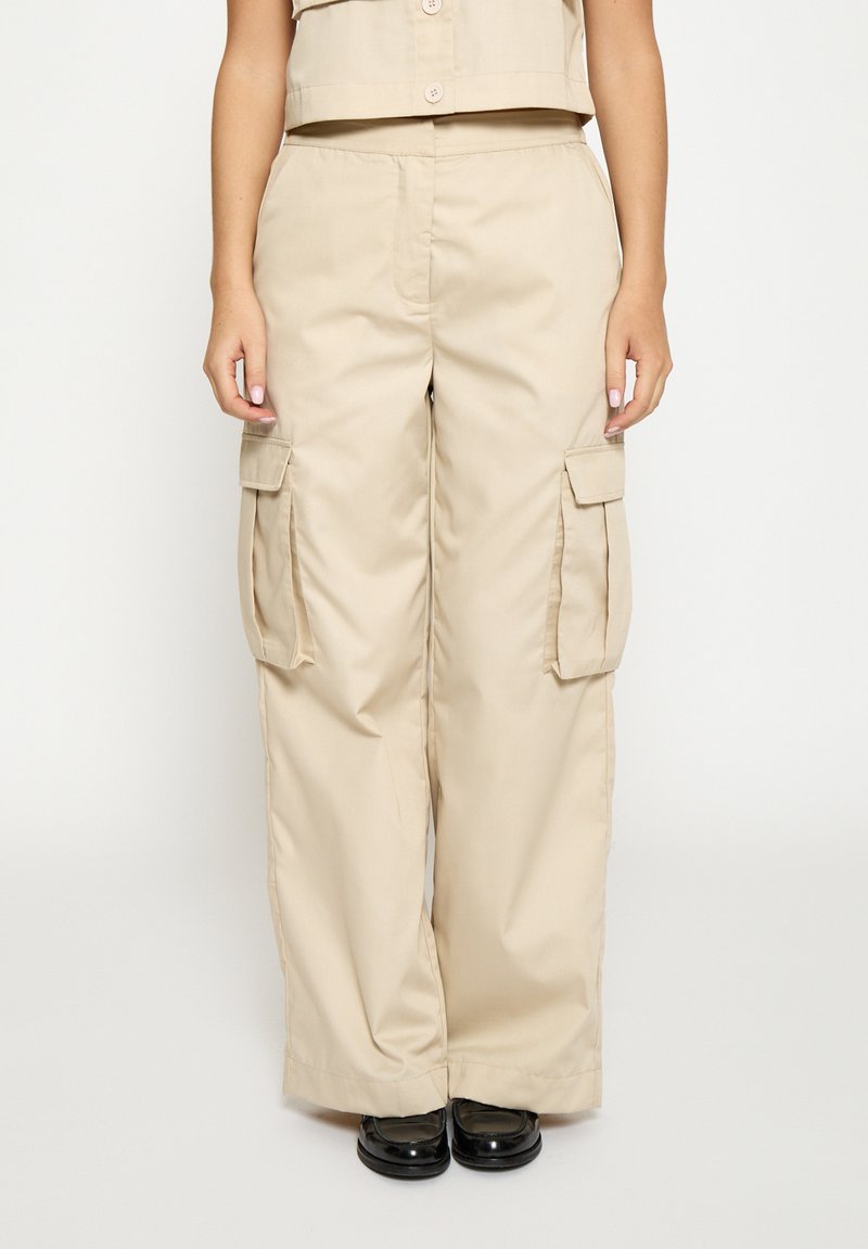 Beige cargobukser lavet af robust stof, med sidelommer, en løs pasform og et lige ben, kombineret med sorte sko.