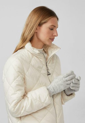 Dikke, gewatteerde jas met hoge kraag en zilveren ritsdetails, gecombineerd met lichtgrijze gebreide handschoenen met een tekstuurpatroon.