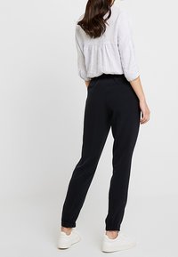 Svarta tapered byxor med elastiska manschetter, gjorda av lätt tyg. Kombineras med en löst sittande, ljusgrå blus. Enkelt design, inga mönster synliga.