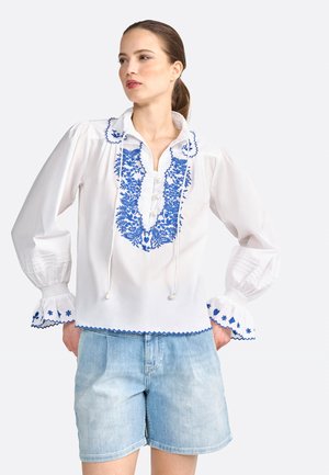 Valge pluus siniste tikanditega lillemustriga, nööbiplakk, stringiga kaelus ja kellukesekujulised varrukad dekoratiivse äärisega. Kombineeritud denim-lühikeste pükstega.