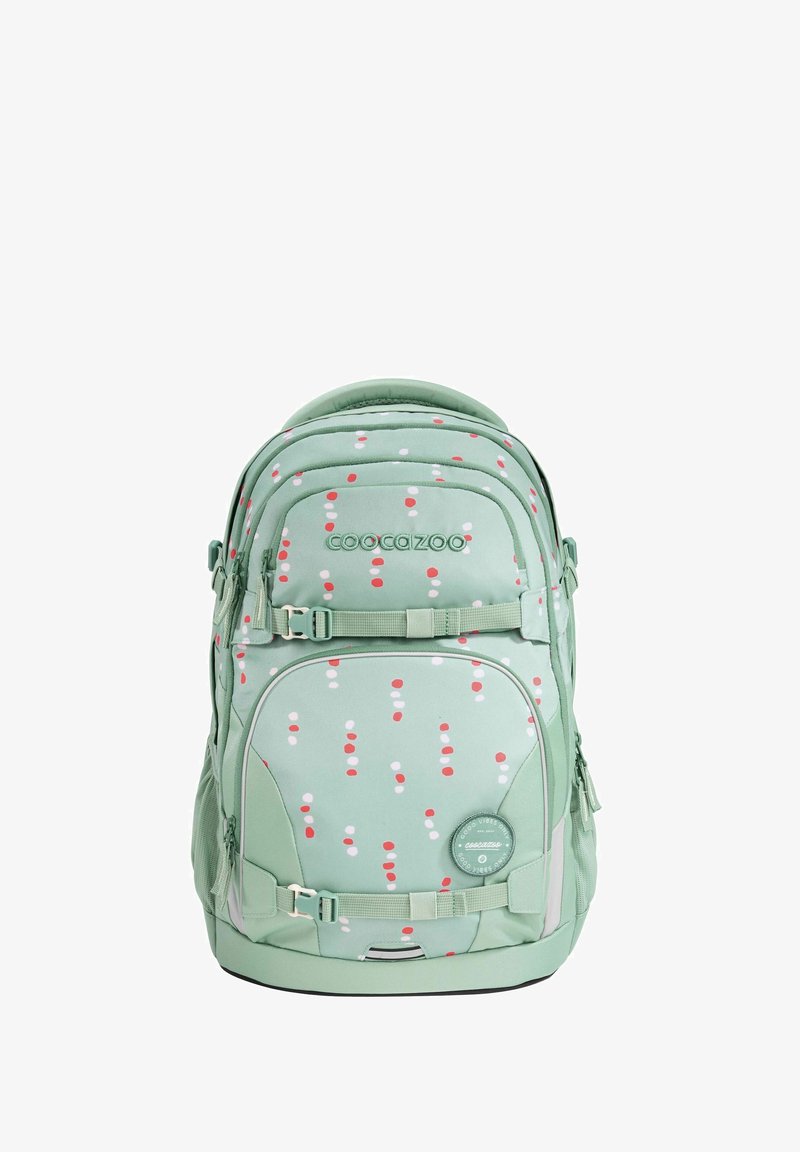 Green backpack with a polka dot pattern in red and white. Features zippers, straps, and a round logo patch. Soft fabric with padded grips.