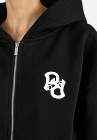 Felpa nera con zip realizzata in tessuto misto cotone. Presenta una tasca a marsupio, cappuccio con drawstring e un logo grafico bianco sul petto sinistro.