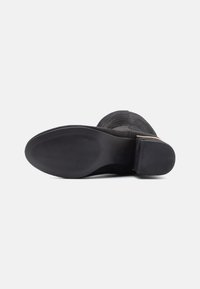 Stivale alla caviglia in suede nero con tomaia texturizzata, punta rotonda e tacco impilato. La suola in gomma presenta un motivo a ondulato per una migliore aderenza.