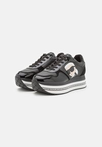 Sneaker nere con accenti in vernice e camoscio, dotate di una grafica stilizzata di un volto, suola intermedia bianca spessa e suola esterna in gomma testurizzata.