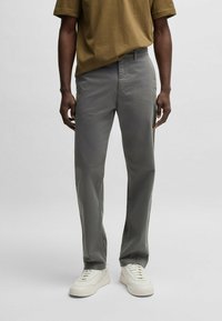 Chino grigi chiari con vestibilità dritta, in cotone, con tasche frontali. Abbinati a una maglietta marrone e sneakers bianche.