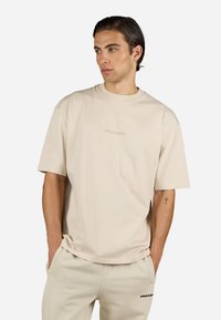 Beige oversized t-skjorte i myk bomull med rund hals, med en subtil "PEGADOR" logo i en matchende nyanse over brystet.