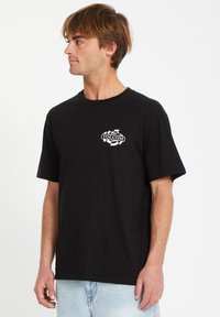 Schwarzes T-Shirt mit kurzen Ärmeln aus Baumwolle. Auf der Vorderseite befindet sich ein weißes Volcom-Logo, umgeben von einem strukturierten Design. Standard Passform und Rundhalsausschnitt.
