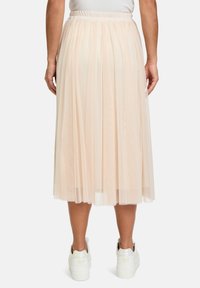 Gonna midi in tulle beige chiaro con vita elastica, design a strati e una texture leggermente trasparente. Indossata con sneakers bianche.