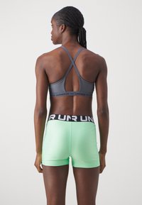 Sujetador deportivo gris con tirantes cruzados en la espalda, combinado con pantalones cortos deportivos de color verde menta que tienen una cinturilla negra con letras blancas.