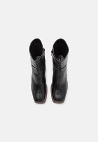 Sorte skinnankelsko med en strømlinjeformet design, firkantet tå og glidelås på siden. Jevn tekstur og subtile sømdetaljer langs sidene.