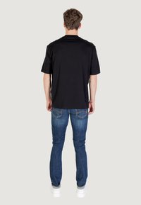 T-shirt nera a maniche corte, vestibilità comoda, abbinata a jeans in denim blu. La t-shirt ha una texture liscia, un design casual e non presenta loghi visibili.