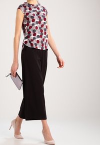Top de manga corta con fondo blanco y lunares rojos y azul marino; combinado con pantalones anchos negros y tacones rosa pálido, sosteniendo un clutch.