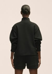 Sudadera negra con cuello alzado, hombros caídos y puños elásticos, combinada con pantalones cortos a juego. Tela suave con diseño minimalista.