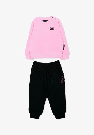 Sweat-shirt rose à manches longues avec lettrage noir "JR", associé à un pantalon de jogging noir avec cordon et texte rose subtil sur la jambe.