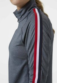 Maglia atletica grigia con zip al collo, che presenta una silhouette aderente, un tessuto strutturato e strisce a contrasto rosse, bianche e blu lungo le maniche.