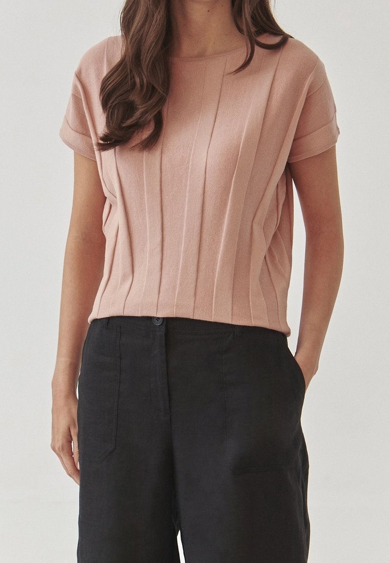 Růžový pletený top s krátkým rukávem, s vertikální žebrovanou texturou, kulatým výstřihem a mírně volným střihem, spojený s černými kalhotami s vysokým pasem.