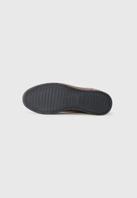 Semelle en cuir brun avec une semelle extérieure en caoutchouc noir texturé. Présente des rainures horizontales et un embout arrondi. Design épuré et minimaliste.