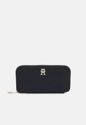 Black zip-around wallet in smooth fabric, featuring a gold logo on the front and a contrasting zipper pull with brand colors.