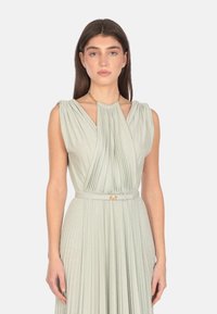 Abito plissettato senza maniche in tessuto verde chiaro con una morbida lucentezza. Presenta una cintura con una fibbia dorata e un dettaglio arricciato sul collo.
