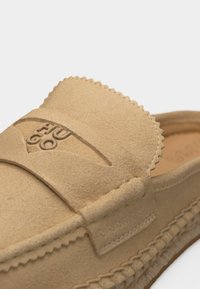 Mocassin beige en daim avec des détails cousus et le logo "HUGO" embossé sur la partie supérieure avant.