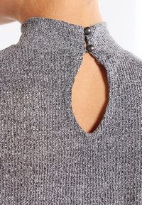 Grå ribbade stickade topp med hög krage och en nyckelhålssömn i ryggen, som hålls fast av två mörka knappar. Mjuk textur och åtsittande form.