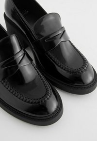 Mustat patenttivahamateriaalista valmistetut loaferit, joissa on kudottu yksityiskohta varpaassa, kohotettu kanta ja sileä pinta. Suunniteltu minimalistisella siluetilla.